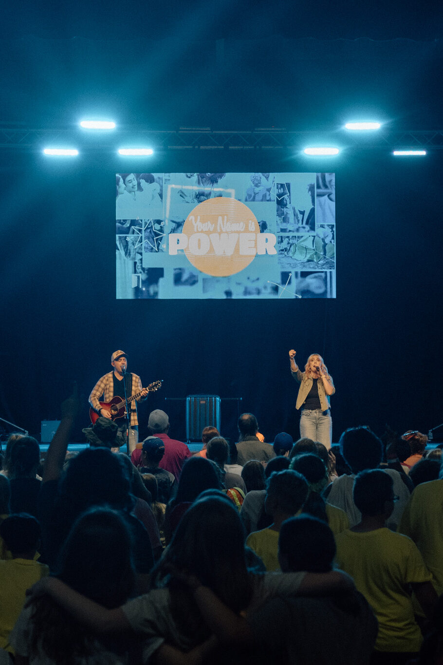 Dave and Jess lead worship on a stage for a large group of kids